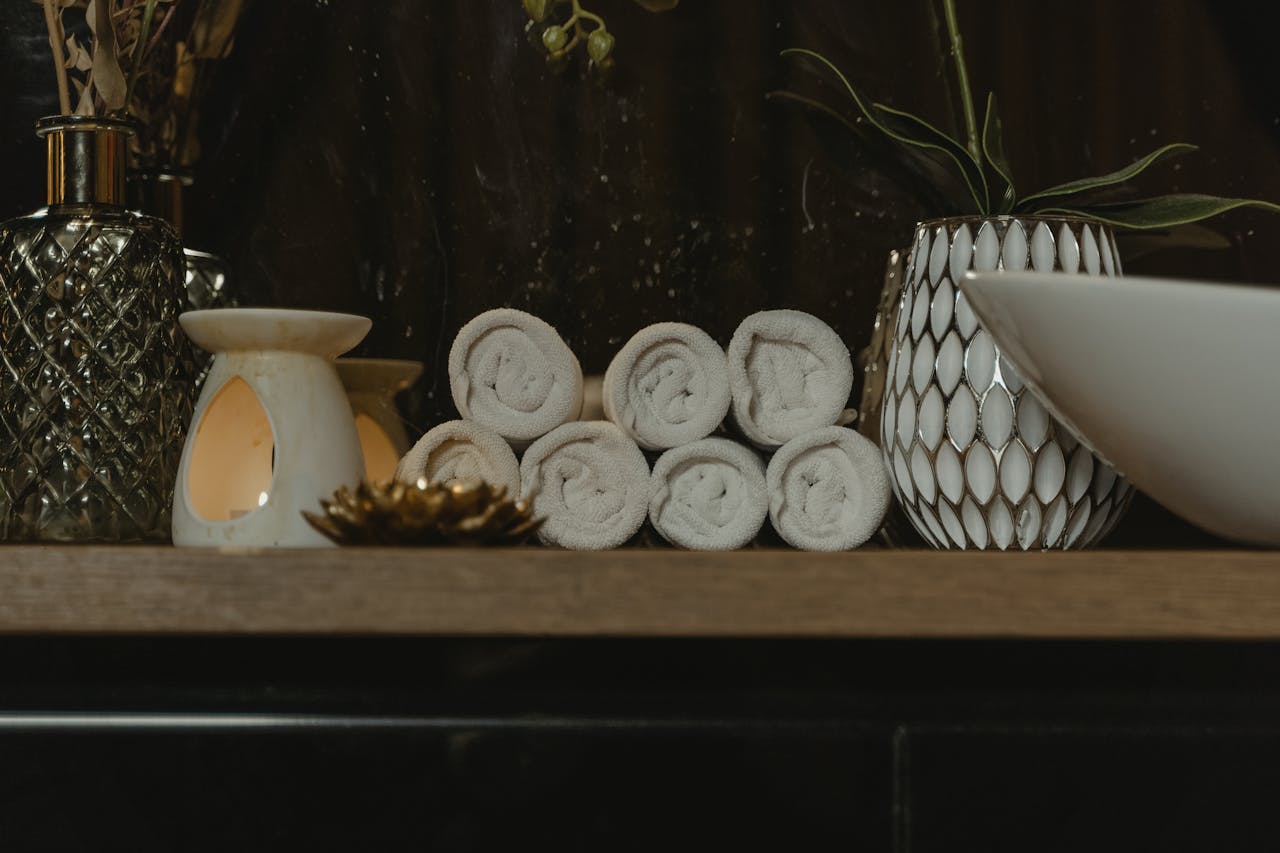 Serene spa setting featuring rolled towels, candlelight, and decorative vases on a wooden shelf.